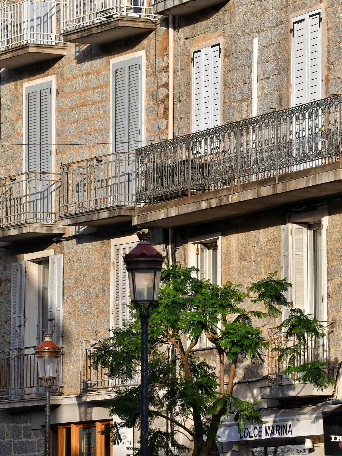 Façade d’immeuble en pierre avec balcons en fer forgé et volets