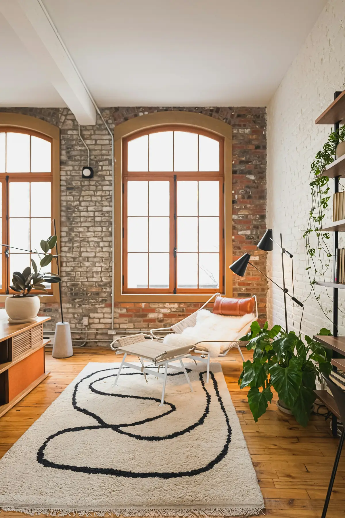 Pièce rénovée avec fenêtres cintrées, mur de briques et parquet